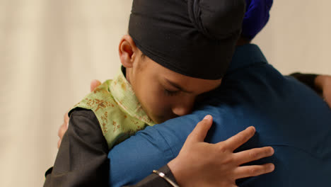 Close-Up-Studio-Shot-Of-Sikh-Father-Embracing-Son-Both-Wearing-Turbans-Against-Plain-Background